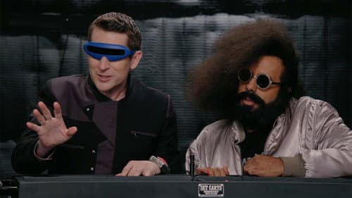 Reggie Watts Wears a Purple and Yellow Quilted Sweatshirt still